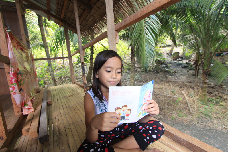Merry Grace Legarde sits reading a letter from her sponsor at home