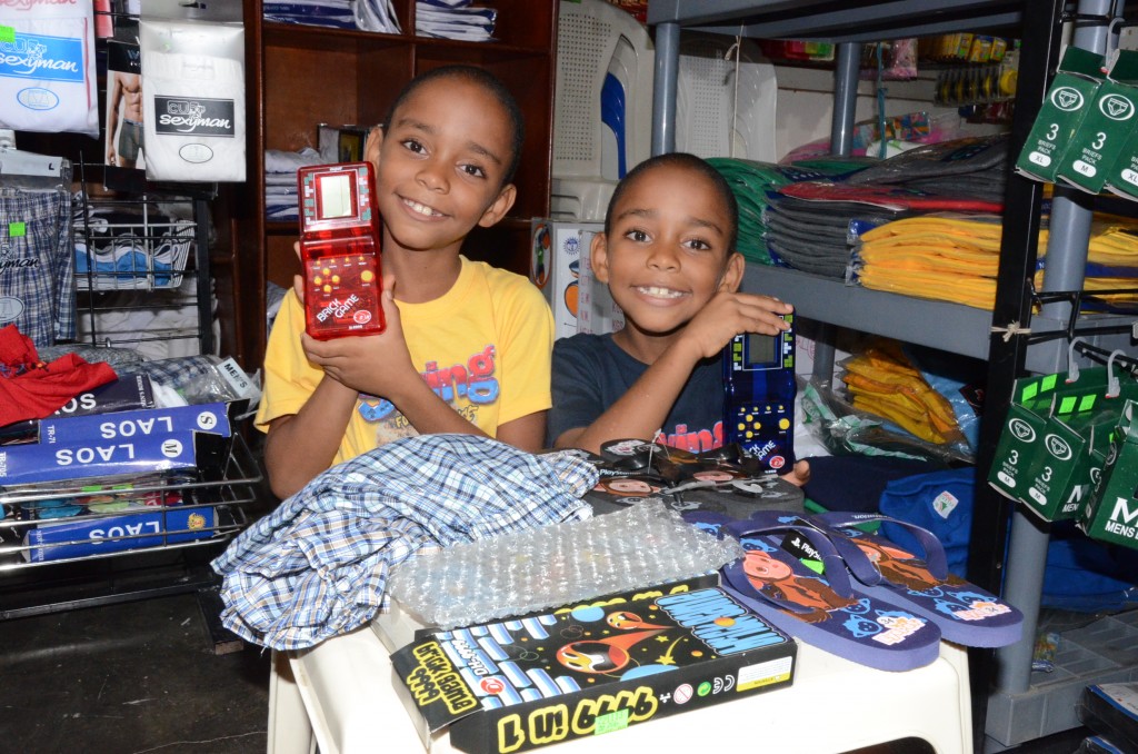 Amauris Jimenez Jimenez and Adoni Jimenez Jimenez smile together standing in a store holding toys on a table with games and clothes