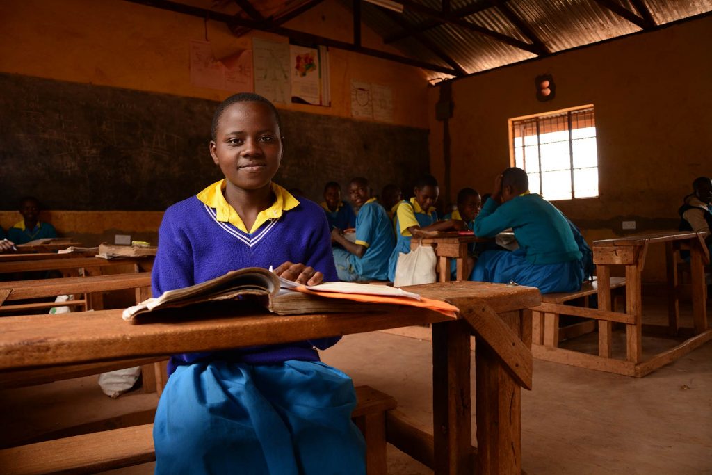 A girl sits at wooden desk in a classroom.