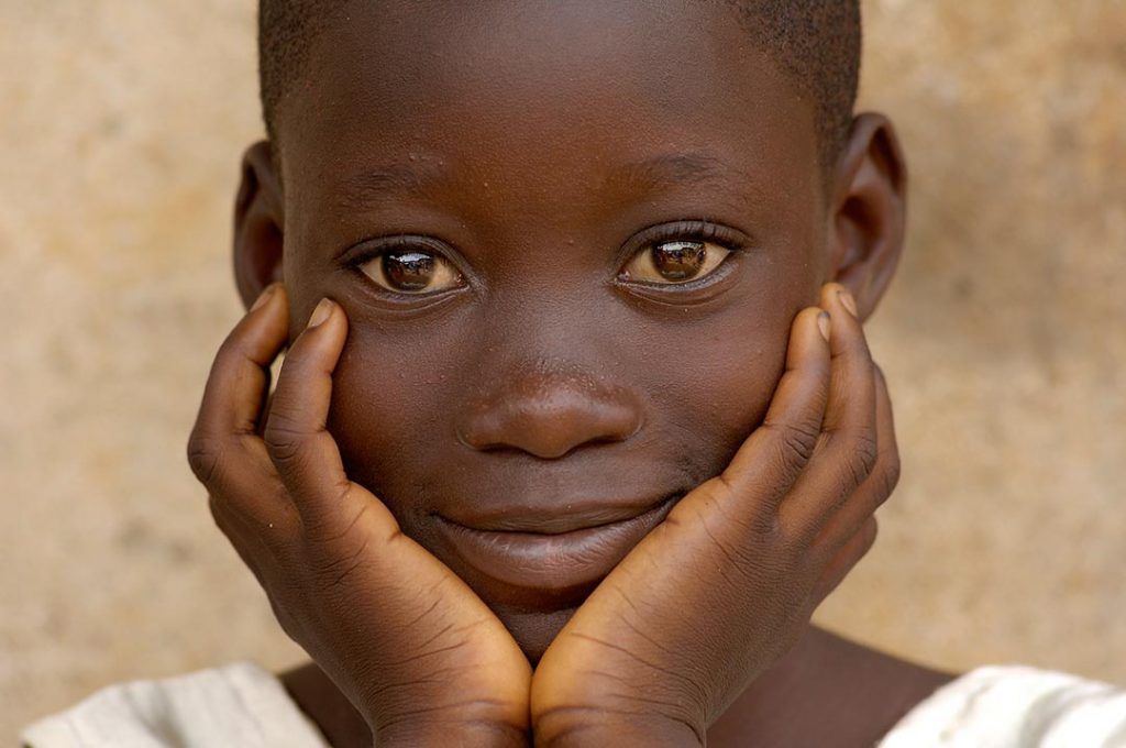 A child looks into the camera and smiles peacefully.