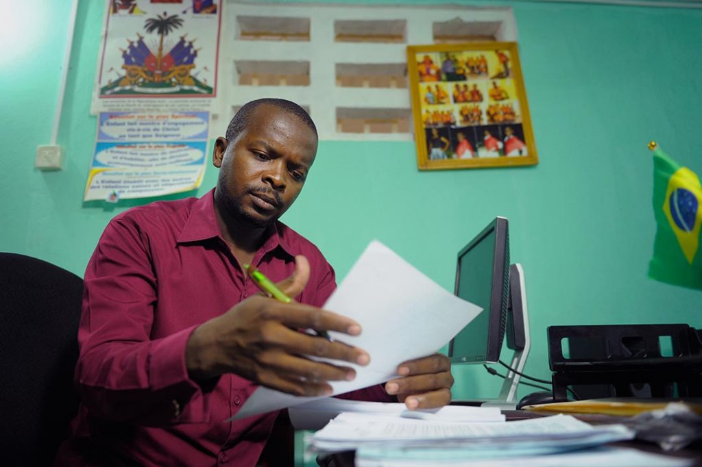 A brazilian man sits at his computer desk and works on paper work.