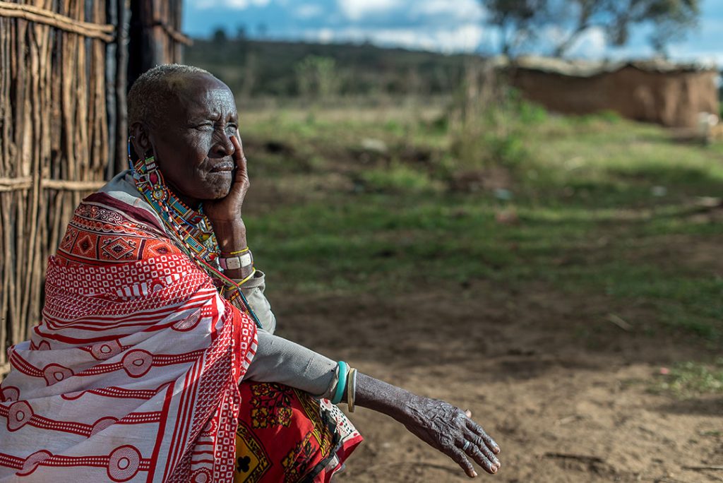 Nasinde, a 75 year old from Kenya, sits in front of her home.