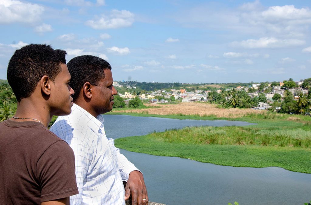 Pablo, a pastor and Compassion centre director, stands with his son Vladimir. They look out over a river near their church.