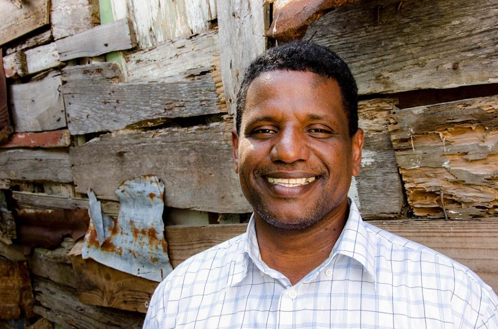 Pablo, now a pastor and director of a Compassion centre, stands in front of a wall and smiles.