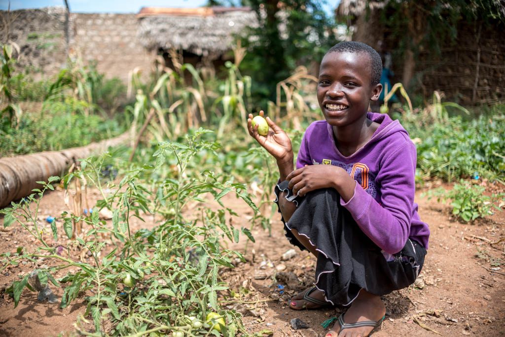 A girl stands in her family garden and holds up some fresh produce.