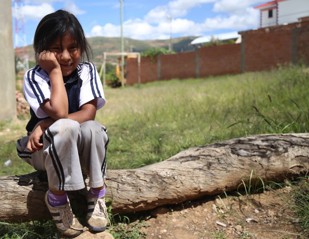 A girls sits on a log in small, grass field.
