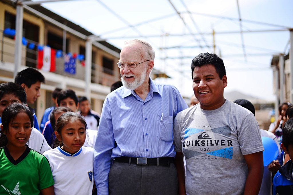 An older man stands at a child center surrounded by kids and leaders.