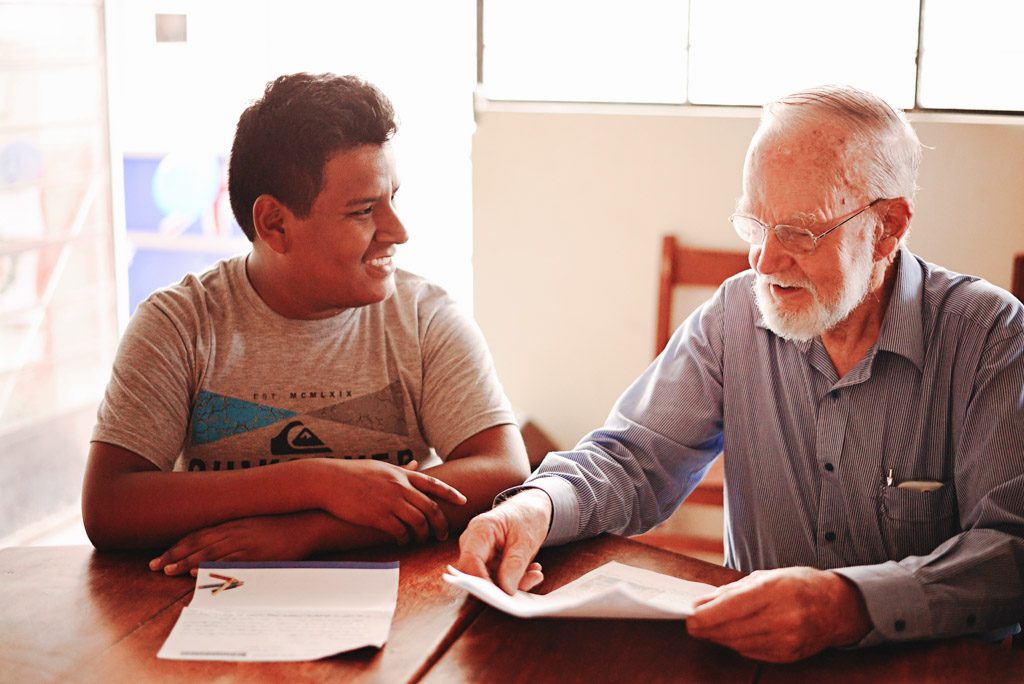 Andrew sits at a desk with his sponsor and reads old letters with him.