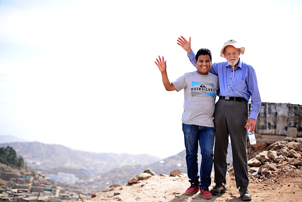 Andrew stands with his sponsor on the top of a hill. They both wave.