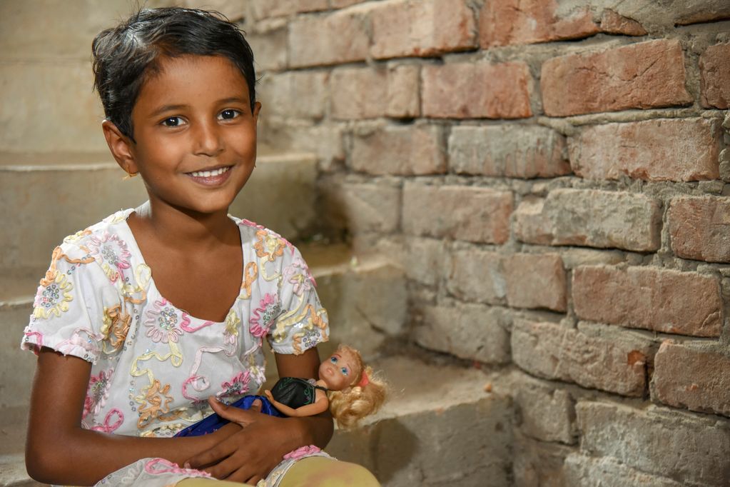 Portrait of a little girl, female child, Ramina beautifully smiling with her doll on the stairways to her brick apartment home.
