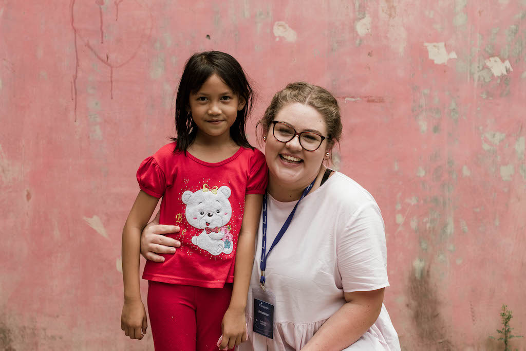 An young Australian woman has her arm around a young Indonesian girl, who is wearing red.