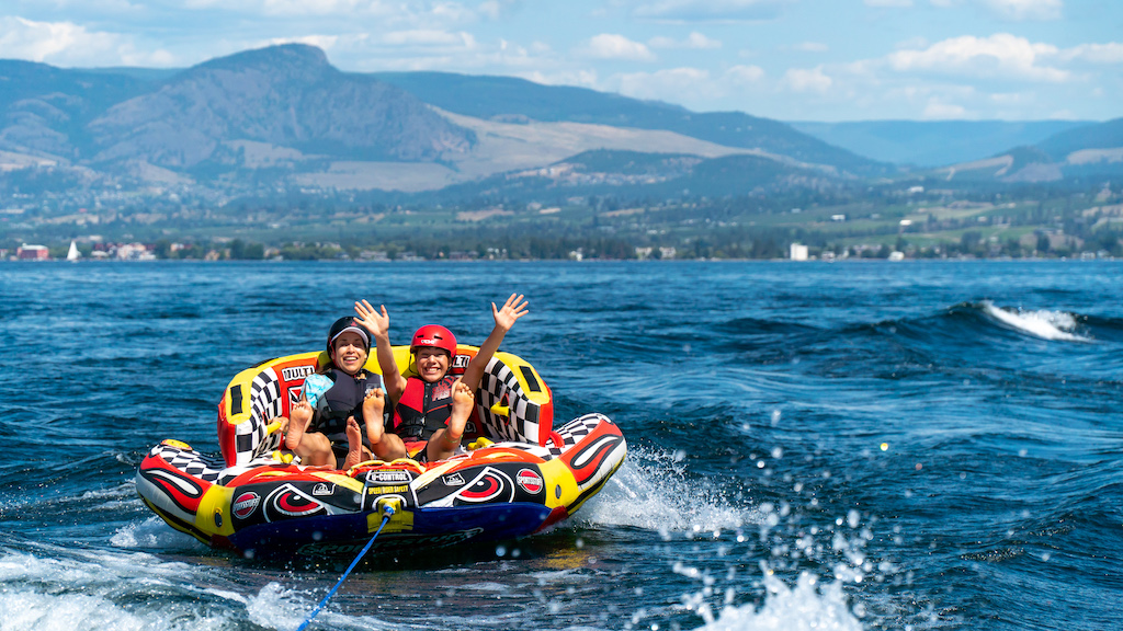 Two individuals on a water tube, wearing helmets and life jackets.