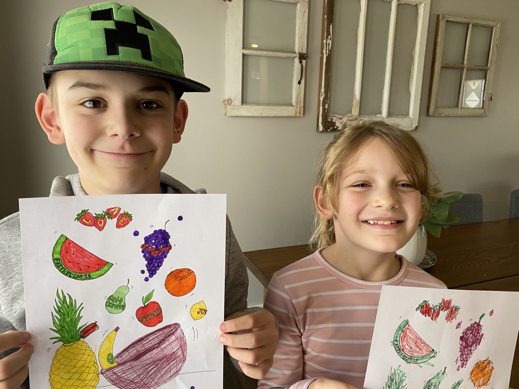 Two kids hold up their finished colouring sheets.