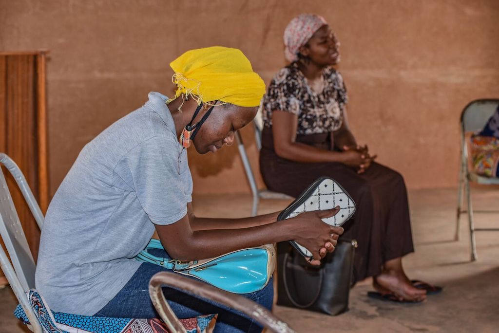 Two volunteers are praying at a weekly prayer meeting at the Compassion centre. The focus is on a woman wearing a gray shirt, yellow head scarf and jeans.