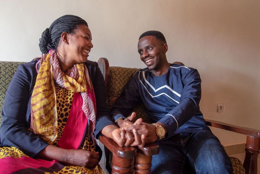 Pascasie and Christian sit together in a living room, smiling.