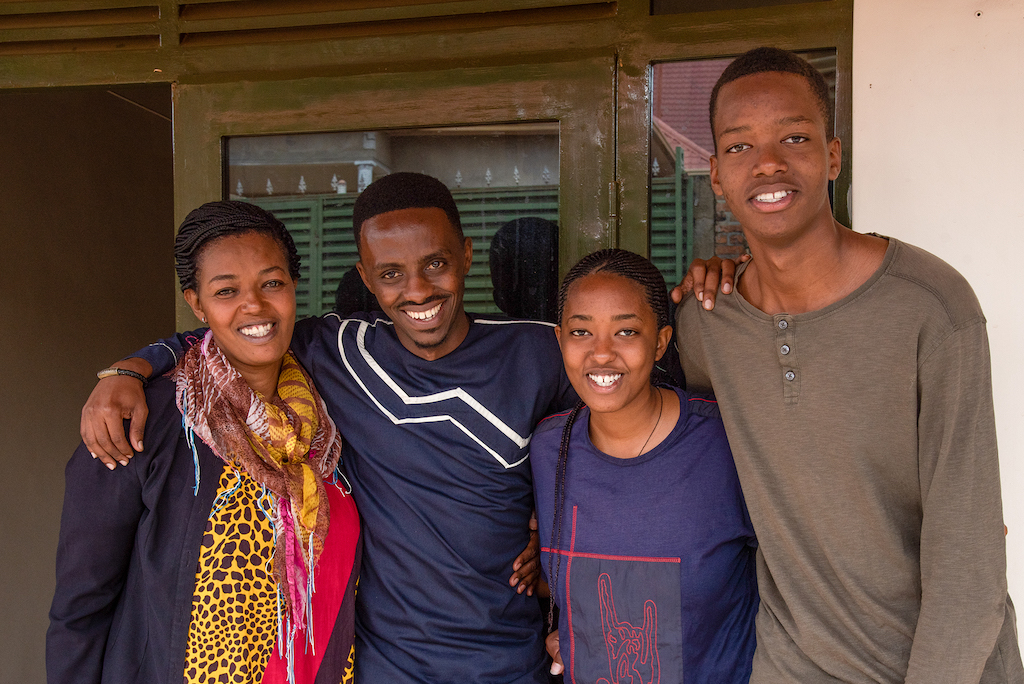 Left to right, Christian's aunt Pascasie, Christian, and his cousins Cynthia and Mugisha stand with their arms around each other.