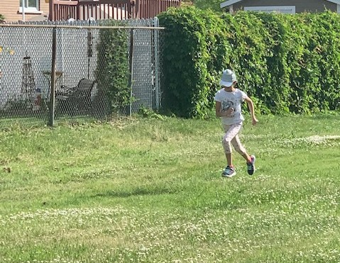 Girl in a white cap is running on the grass