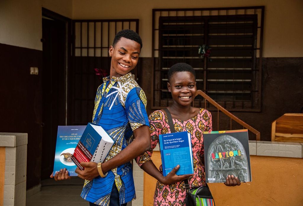 Two teens in Togo stand holding up their textbooks.