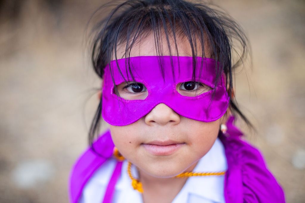 Adaly is wearing a purple mask and cape. She is standing outside.