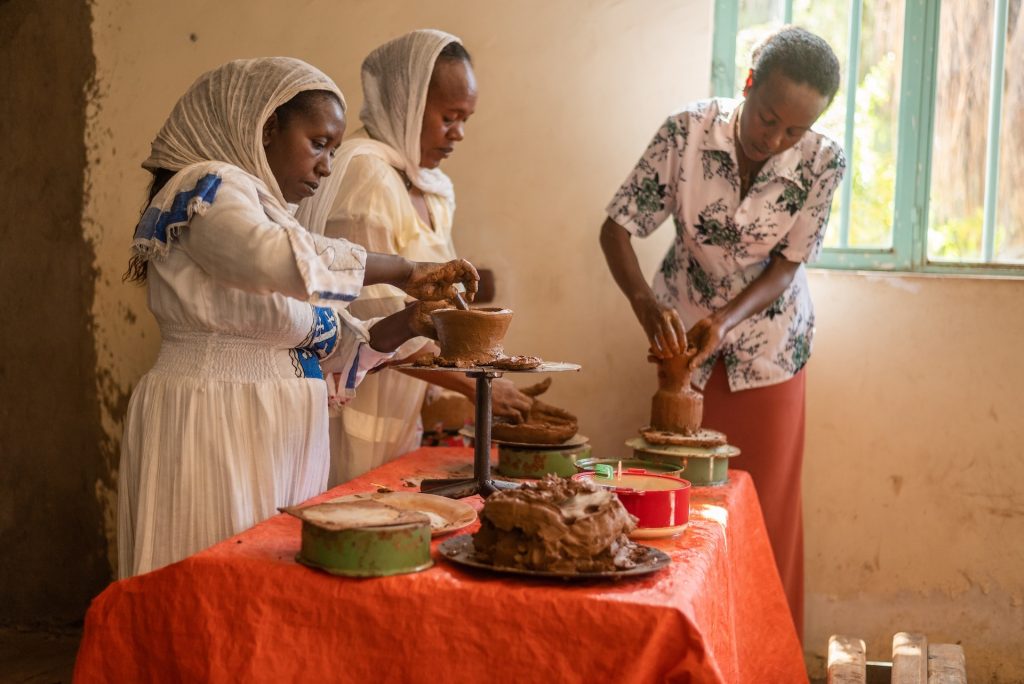 Three mothers are standing at a table making pieces of pottery.