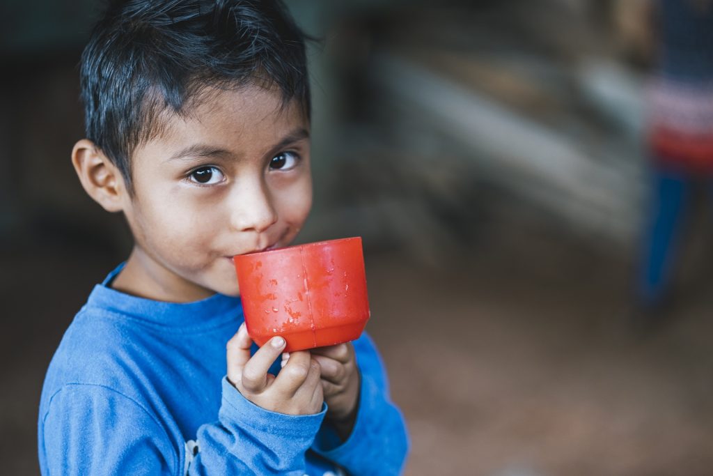 A young boy enjoys a cold drink in a red cup.
