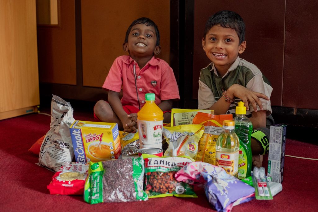 Vengadeshwaram, left, and Vishal, right, are sitting on the floor with the rations they received from the child development centre on the floor in front of them.