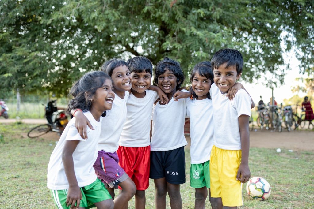 A group of smiling children have their arms around each other.