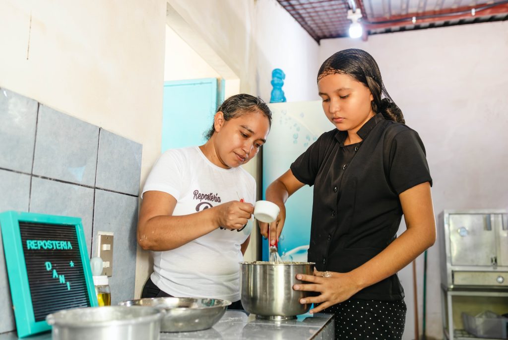 Daniela and her mother Paty inside their pastry kitchen. They are cooking together, preparing the dough for a cake.