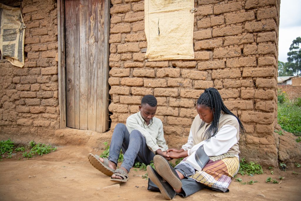 Alinafe and Yamikani hold hands while praying. They are sitting outside of his stone house.