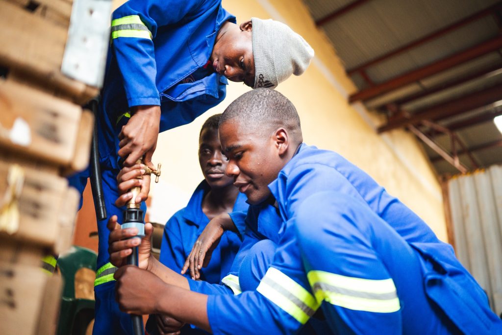 Alinafe and two of his colleagues fix a pipe. They are wearing blue uniforms.