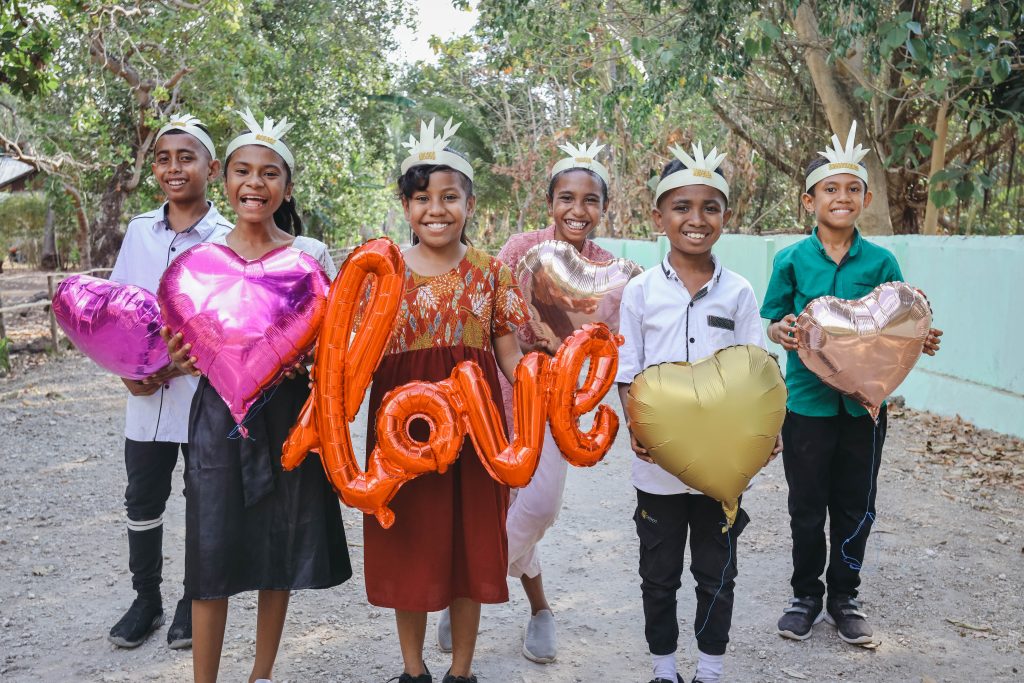 A group of children from Indonesia hold balloons and smile.