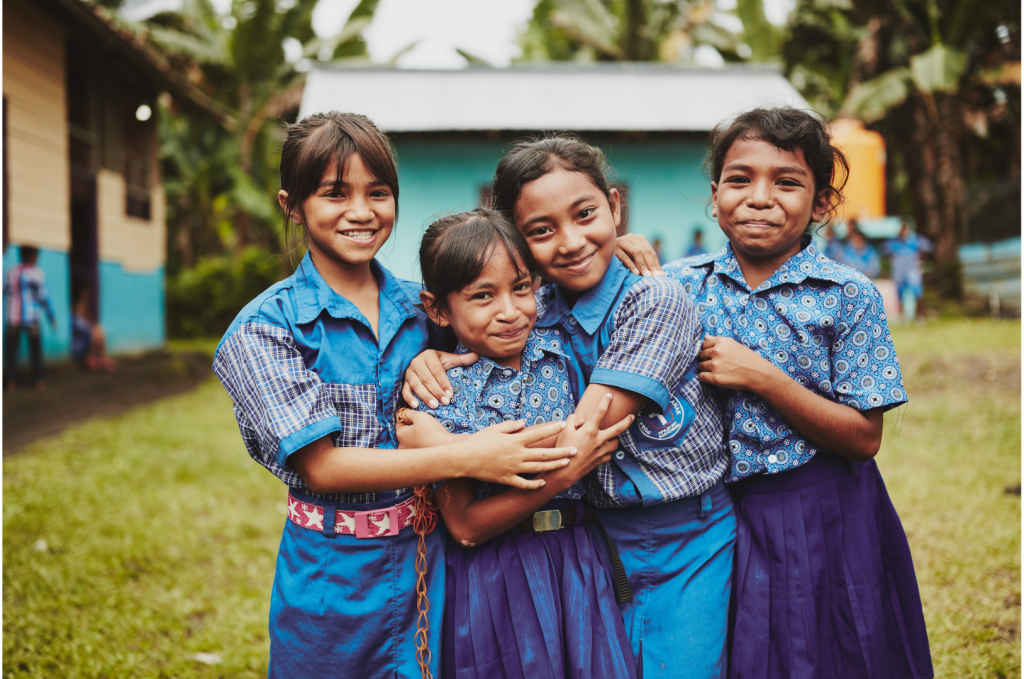 Four girls in blue stand together hugging and smiling.