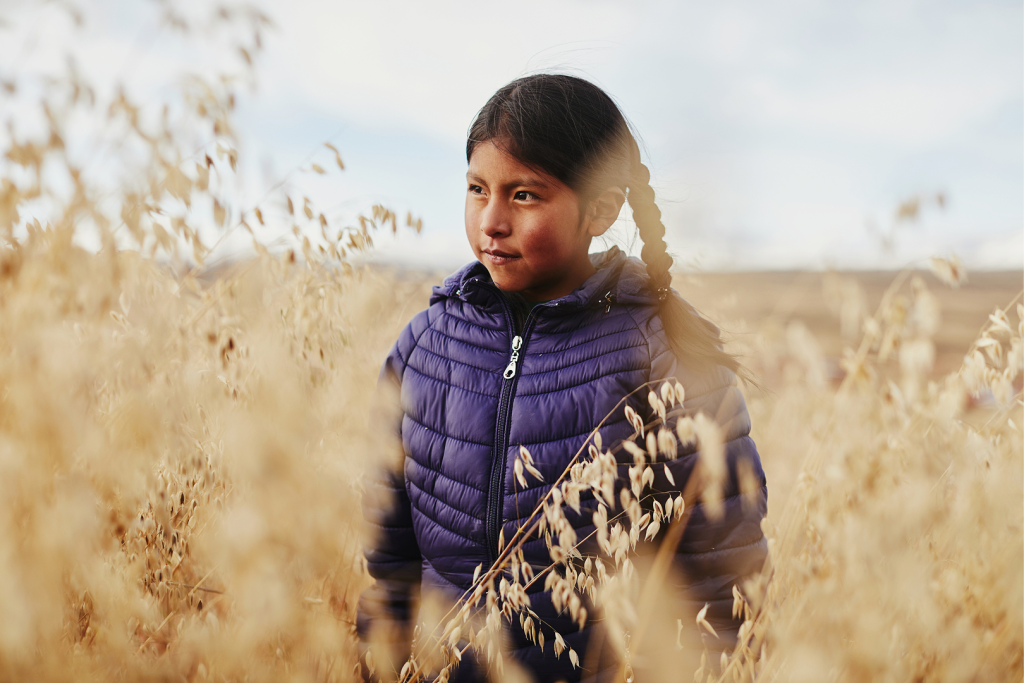 A young girl stands in a field. She has her hair in two braids.