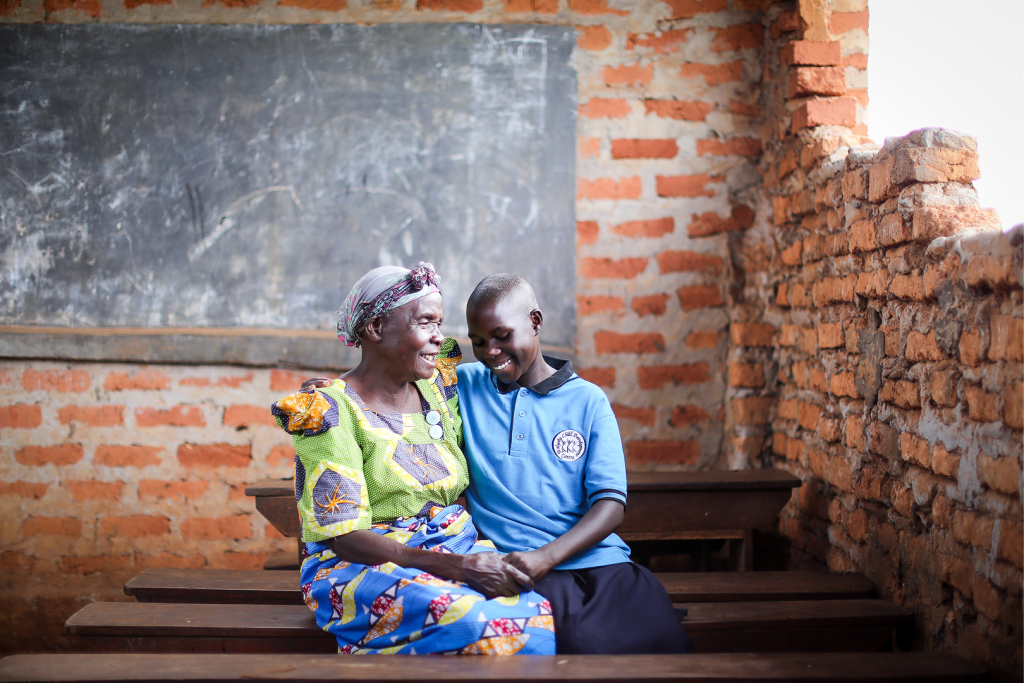 An older woman sits holding the hand of a young teenage girl in a classroom.