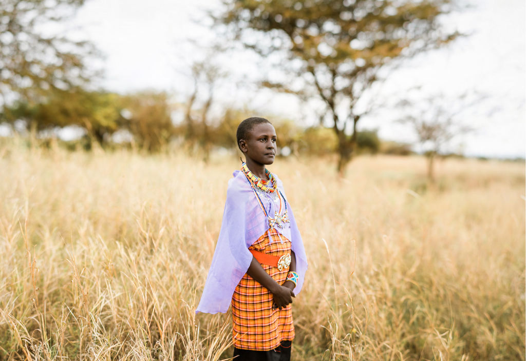 A teenage girl stands in a field holding her hands in front of her.