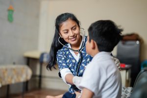 Nurse wearing nurses uniform holding a stethoscope to a little boys chest 