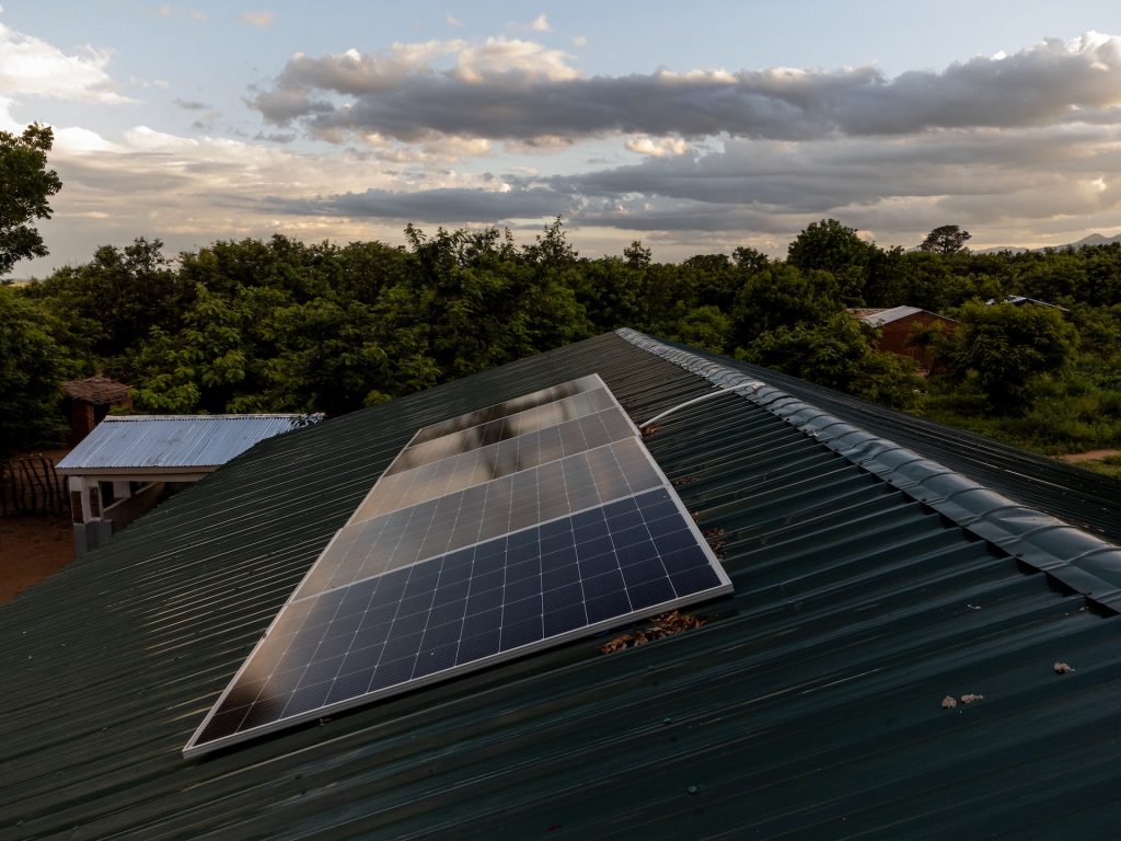 A close up of the solar panels on the roof of the child development centre in Nsanje, Malawi. The panels can be seen on the pitch of the green corrugated roof near the bend. Trees line the background of the building.
