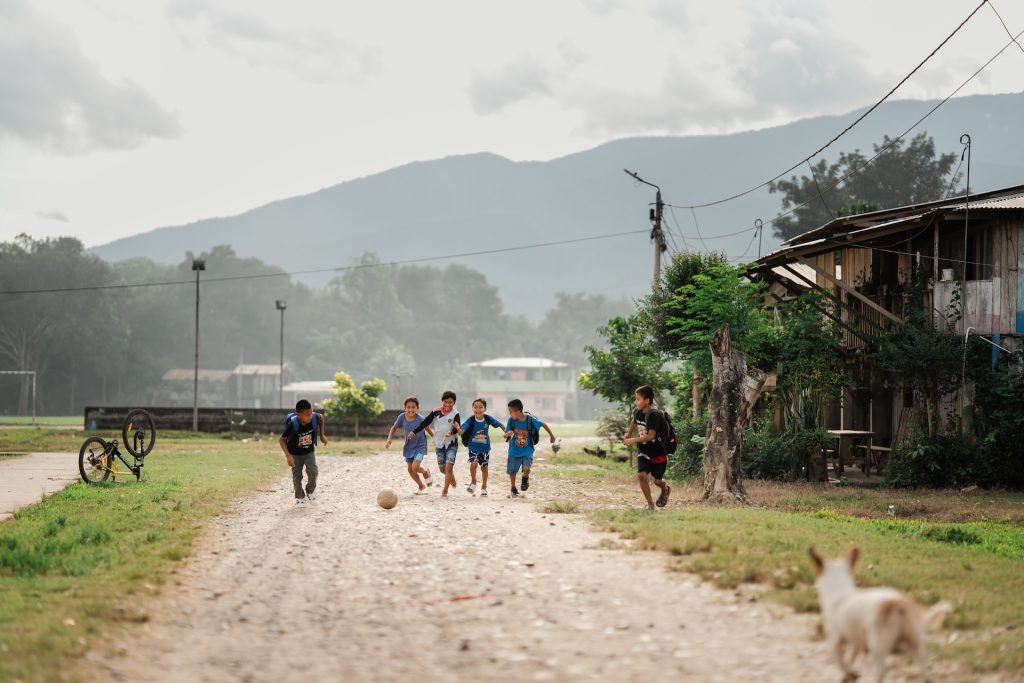 Participants from the centre are having fun in their community. The group of boys are running down a dirt path kicking a soccer ball.
